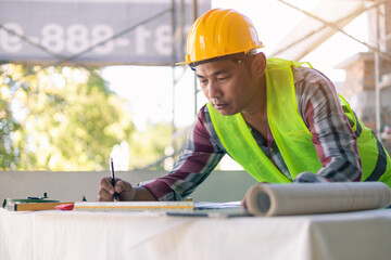 Asian architecture designing blueprint planning using pencil tool drawing, working in construction site, engineer worker building innovation analyzing planning, wearing safety vest and helmet gears.