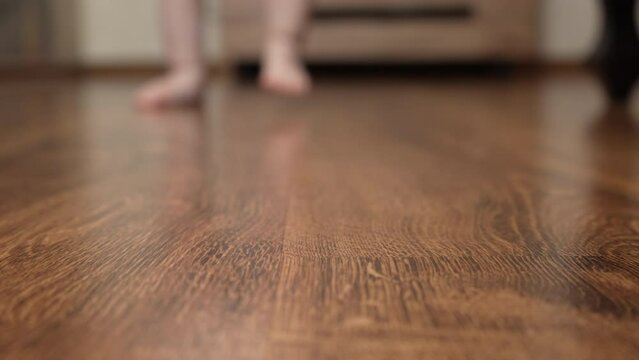 The baby's bare feet stomp on the parquet floor. Close-up. Blurred background. Slow motion. An unrecognizable baby walks barefoot on a wooden parquet floor. 4k footage