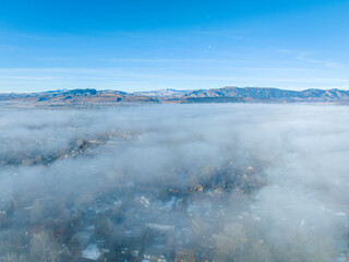 foggy winter morning over residential area of Fort Collins in northern Colorado after heavy rain and snow, aerial view with Front Range of Rocky Mountains in background