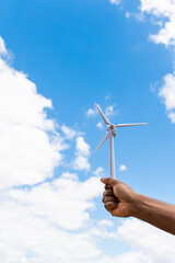 Hand of a young African man holding a model of wind turbine generator against the sky, symbol of the green renewable energy © vikarayu