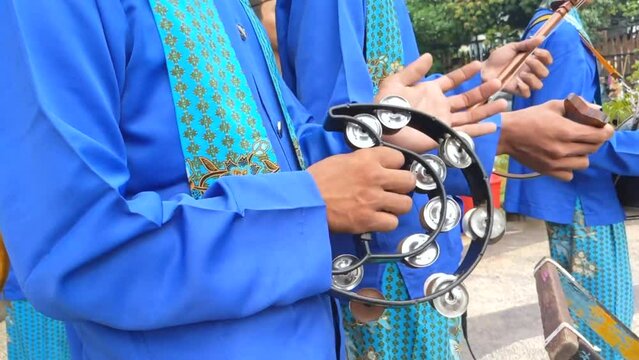 Cinematic shot. A hand of young musician playing double row handle tambourine in the Betawi tribe musical performance.