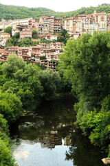 The old town of Veliko Tarnovo is reflecting in the water of the Yantra River, surrounded by dense...