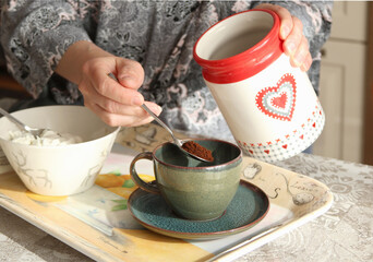 Woman in robe put coffee in cup in kitchen. Valentine's Day. 