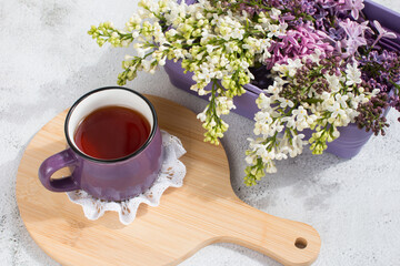 a cup of tea and a branch of lilac on a white background in a basket. Spring Postcard