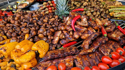 Large round rotating grill with assorted meats and vegetables. Rotary grill. Demonstration of cooked meat, potatoes, mushrooms, zucchini, peppers and tomatoes. Street food. Food court. Fair