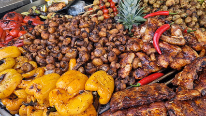 Large round rotating grill with assorted meats and vegetables. Rotary grill. Demonstration of cooked meat, potatoes, mushrooms, zucchini, peppers and tomatoes. Street food. Food court. Fair