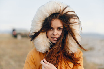 Beauty in nature young woman in orange coat with fur hood standing in field, fashion and travel...