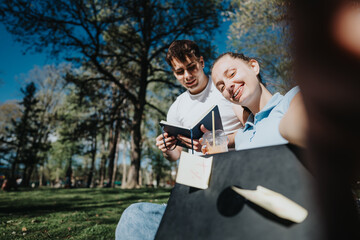 Two high school students study together outdoors on a sunny day, collaborating on a project with...