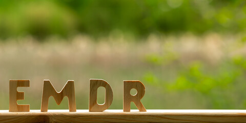 Letters EMDR cut out of wood. Small forest pond with fluffy cattail in blurred background. Eye...