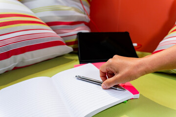 Close up of hand taking pen with blank agenda and tablet in the background loading with a youthful and restful environment for study f