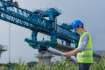 worker on the construction site with Beam Launcher on Background.  engineer  in hand hold blue print on railway construction.