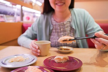 Happy Asian woman eating Sushi at modern Japanese Sushi bar.