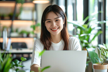 Cheerful young Asian businesswoman working on laptop in office setting with lots of plants and natural light, workplace environment concept, Generative AI