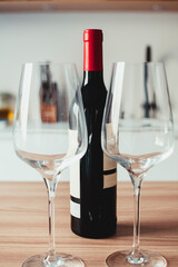 A bottle of red wine is next to two wine glasses on a wooden table