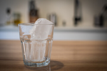A glass of water with ice in it sits on a wooden table