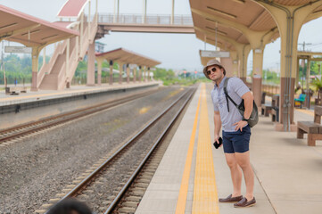 Handsome young man with a backpack uses the phone while standing near the railroad train on the platform,Tourism and travel in the summer. Vacations for the student.