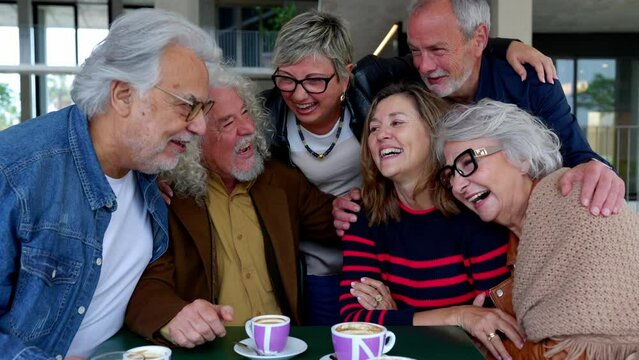 Joyful group of senior friends having fun drinking coffee at cafeteria bar. Baby boomer generation people laughing bonding while having breakfast together at coffee shop. Elderly lifestyle concept.