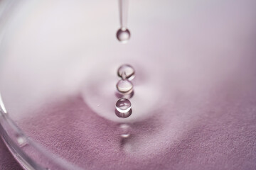 Serum or cosmetic oil flows into a transparent bowl on a purple background.