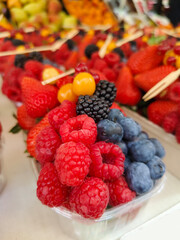 Colourful and healthy fresh berries fruit in plastic bowl at street food market. Spot focus.