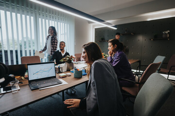 Multicultural group of young business professionals discussing growth and statistics using graphs during a meeting in a contemporary office setting.