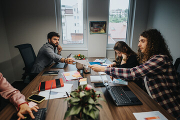 A multicultural team of young workers engaged in a brainstorming session at a cluttered office table, analyzing charts and discussing project ideas enthusiastically.