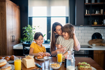 Small adorable boy and girl with beautiful smiling mother enjoying breakfast at home in the morning.