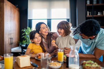 Adorable small boy and girl with beautiful caring parents sitting at kitchen table enjoying breakfast at home in the morning. Family meal at home.
