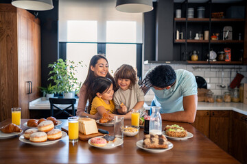 Small cute kids with two parents sitting at kitchen table enjoying breakfast at home in the...