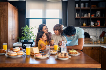 Adorable small boy and girl at breakfast with caring parents in the kitchen at home.