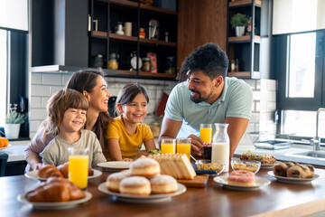 Adorable small boy and girl at breakfast with caring parents in the kitchen at home.
