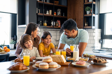 Cheerful young parents talking with their kids during breakfast at home.