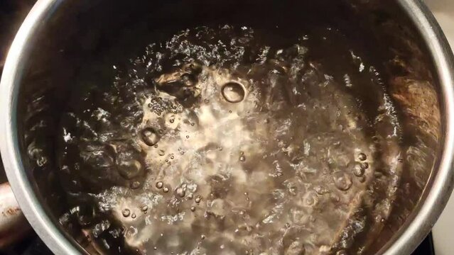 Boiling water with steam rising and bubbles forming in a stainless steel pot
