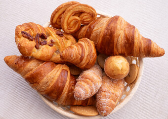 Sweet bakery products and croissant in the basket captured from above (top view), white background