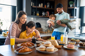 Young mom and daughter spreading marmalade on slice of bread for breakfast while dad is playing with son in the background.