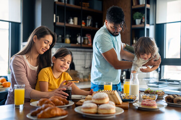 Mother and father at breakfast with son and daughter in the kitchen at home.