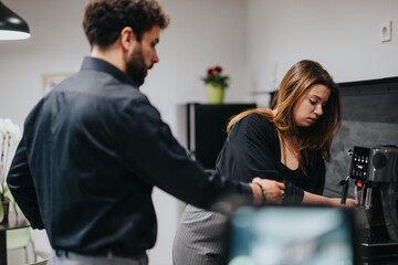 Two coworkers engage in a light conversation while making coffee in a well-equipped office kitchen, highlighting a moment of rest and togetherness amid the busy workday.