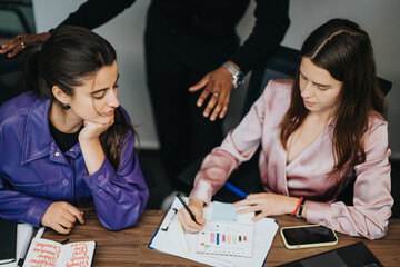 Fototapeta premium In the office environment, two professional women engage in a focused, strategic discussion over business analytics, demonstrating effective teamwork and collaboration.