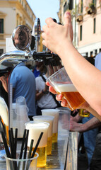 Busy bartender is pouring a plastic glass with ice-cold blonde beer