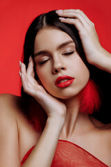 Obraz premium Brunette woman and red feather earrings on a red background. Portrait of a model with bright makeup and red lipstick.