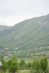 Obraz premium Beautiful landscape view of the Norwegian mountains at the foot of which are wooden Scandinavian-type colorful private houses on a foggy rainy summer day