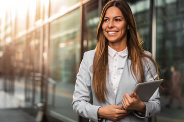 Attractive young businesswoman standing alone outside an office building with digital tablet.