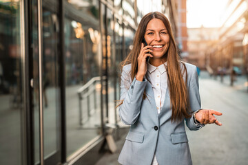 Attractive businesswoman talking on the phone while walking down the city street. Stylish woman...