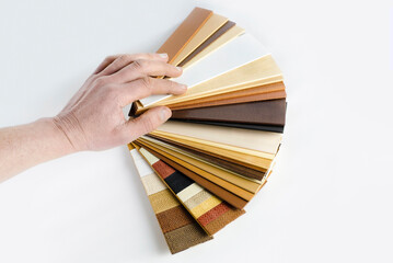 A fan with samples of wooden window blinds on a light background, a man chooses wood material to...
