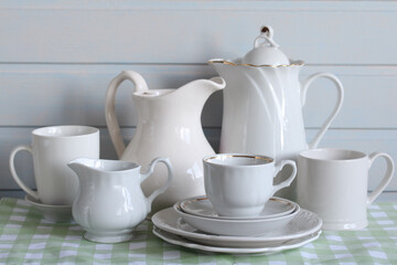 white dishes on a checkered tablecloth on the table in close-up. jug and coffee pot, cup and mug, various plates.