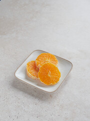 three juicy slices of fresh orange on a square plate on a cream-colored stone backgrounds. Copy space.
