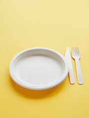 Disposable eco-friendly tableware.Empty recycled cardboard plate and wooden cutlery for take-away food. Plastic free. Copy space on yellow background.