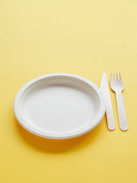 Disposable eco-friendly tableware.Empty recycled cardboard plate and wooden cutlery for take-away food. Plastic free. Copy space on yellow background.
