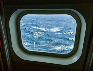 Naklejka premium Porthole view of North Pacific Ocean as seen from deck 8 cruise ship. Waves have white caps showing rough seas. Ship's rail can be seen below. Good framework outlines water movement.