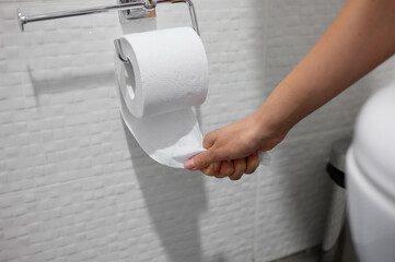 Close-up of woman hand pulling from roll of toilet paper hanging on wall, tearing piece of paper....