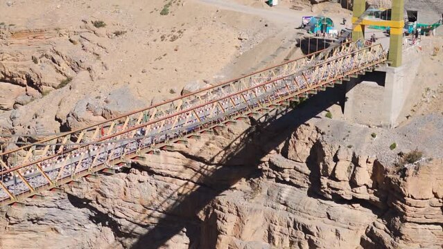 Handheld shot of a bike crossing the Chicham bridge above the mountain valley between Chicham and Kibber villages near Kaza in Spiti Valley, Himachal Pradesh, India. Biker crossing suspension bridge.